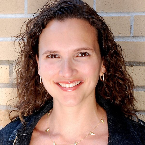 Portrait+of+a+woman+with+medium+length+dark+hair+smiling+against+a+brick+wall.